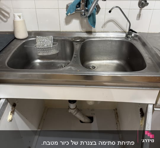 כיור מטבח עם ברזים וצנרת גלויה מתחת